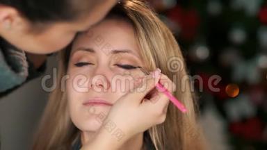 漂亮的化妆师在模特眼上应用眼线特写。 化妆品眼影。 化妆用眼线刷